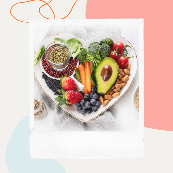A heart-shaped bowl filled with vegetables, fruit, grains, and beans