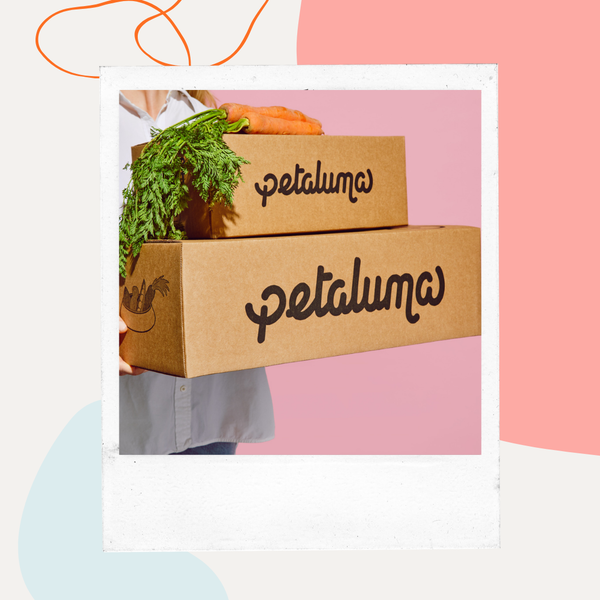 Person holding Petaluma shipping boxes topped with fresh greens