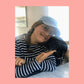 Woman wearing the light blue Petaluma hat cheek to cheek with a black dog
