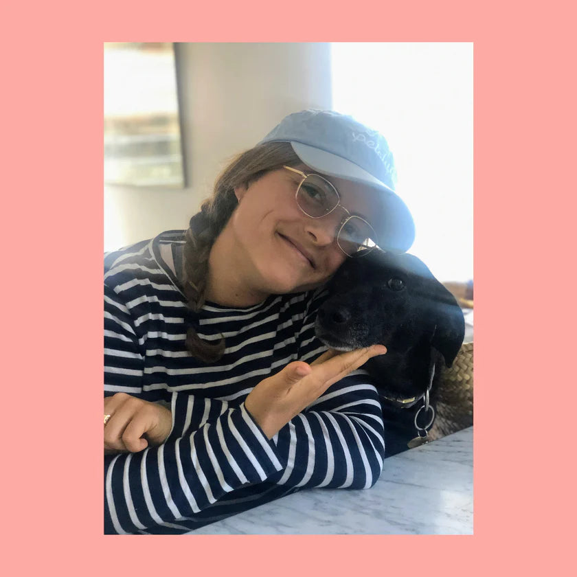 Woman wearing the light blue Petaluma hat cheek to cheek with a black dog